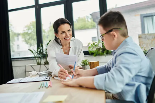 Una madre sorride a suo figlio mentre entrambi lavorano in una scrivania nel loro ufficio di casa. — Foto stock