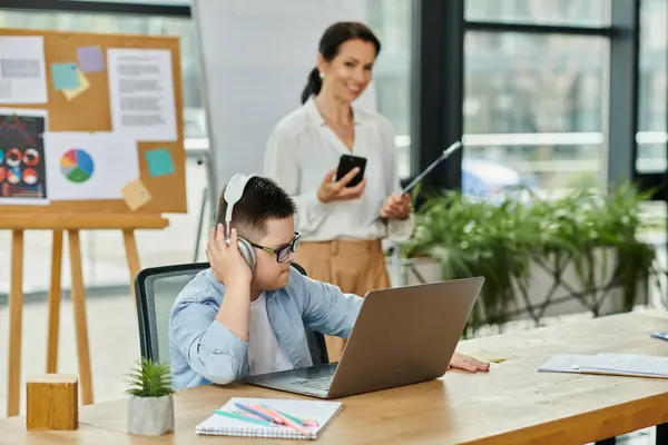A young man with Down syndrome works on his laptop while his mother works nearby, showcasing inclusivity and diversity in the workplace. — Stock Photo