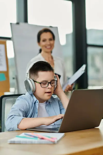 A boy with Down syndrome uses a laptop while his mother watches nearby, showcasing inclusivity and diversity in the workplace. — Stock Photo
