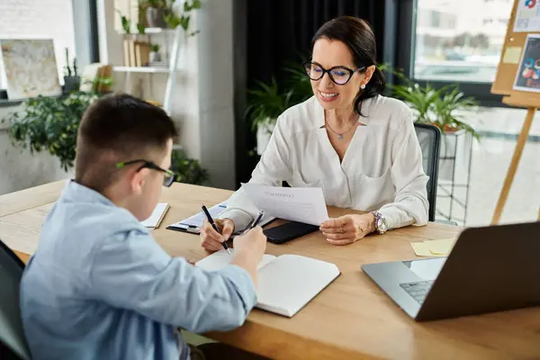 Eine Mutter und ihr Sohn mit Down-Syndrom arbeiten an einem Schreibtisch in einem Büro und setzen sich für Inklusion und Vielfalt ein. — Stockfoto