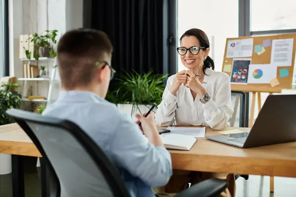 A mother works at her desk in an office with her son, who has Down syndrome. — Stock Photo