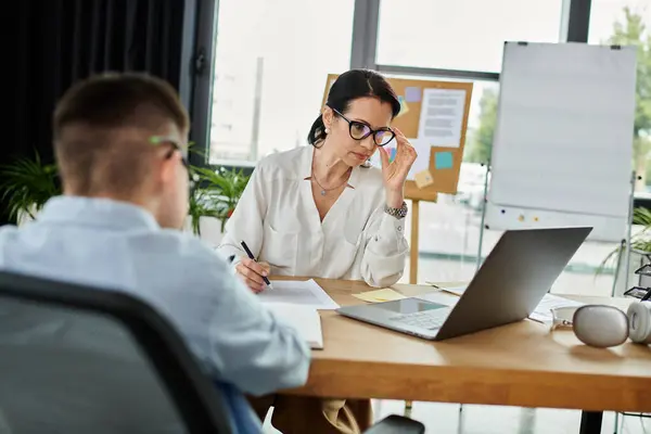 A mother works at her desk in an office, while her son sits beside her. — Stock Photo