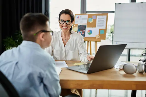 A mother working in her office smiles at her son with Down syndrome, showcasing a beautiful moment of connection and inclusivity. — Stock Photo