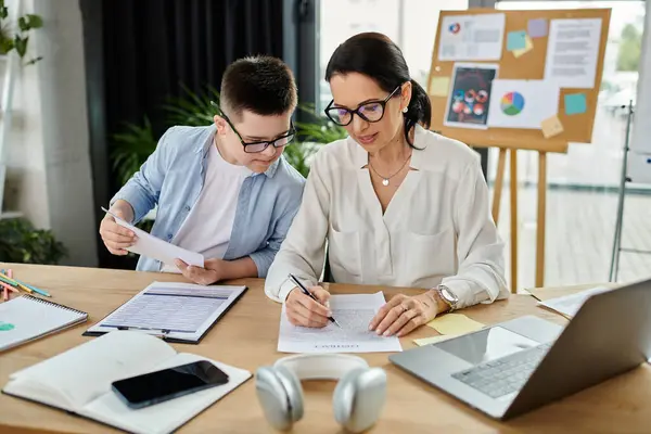Eine Mutter arbeitet an ihrem Laptop, während ihr Sohn mit Down-Syndrom beobachtet, was die vielfältige Einbeziehung der Familie am Arbeitsplatz demonstriert. — Stockfoto