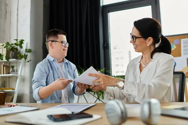 A mother and her son, who has Down syndrome, work side-by-side in an office setting, sharing a lighthearted moment. — Stock Photo