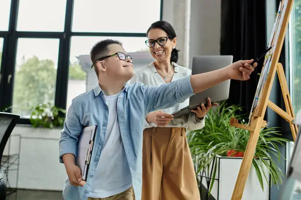 A mother and her son with Down syndrome work together in an office setting, showcasing inclusivity and diversity. — Stock Photo