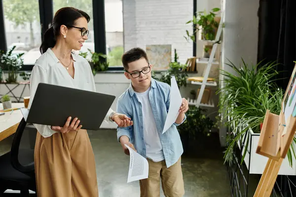 A mother and her son, who has Down syndrome, work together on a creative project in their home office. — Stock Photo