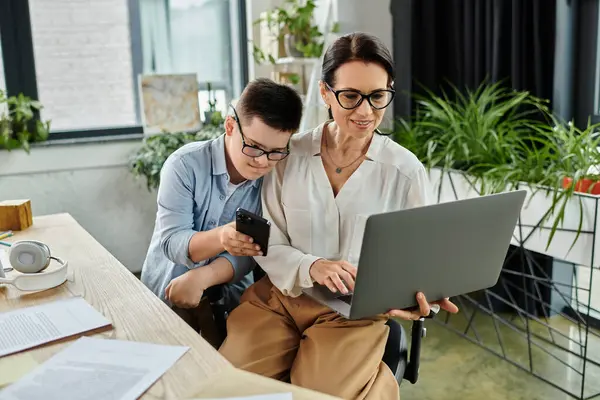 A mother and her son with Down syndrome work side-by-side at a desk, showcasing the importance of diversity and inclusion in the workplace. — Stock Photo