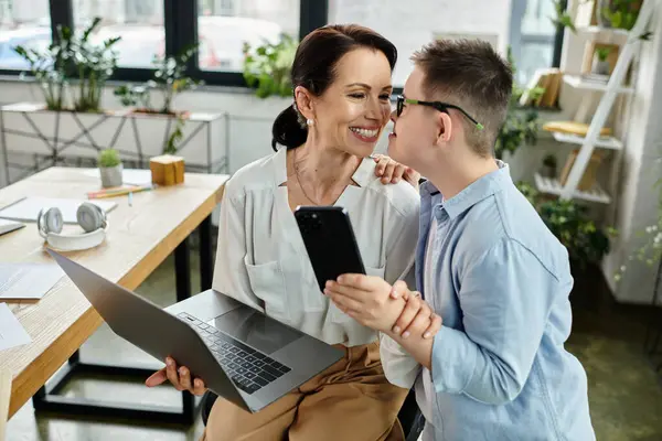 A mother works on her laptop while her son with Down syndrome leans in for a loving hug. — Stock Photo