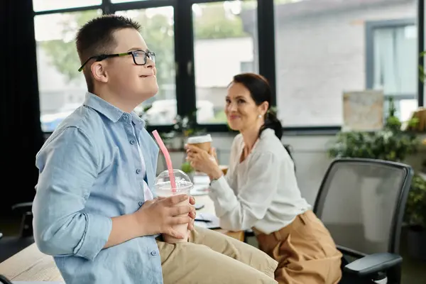 A mother and her son, who has Down syndrome, are taking a break in the office, enjoying a drink and each others company. — Stock Photo