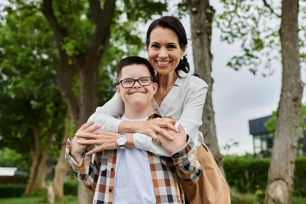 A mother embraces her son with Down syndrome while walking in a park near an office building. — Stock Photo