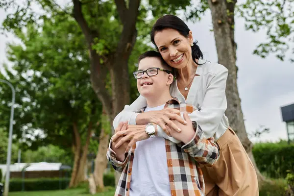 Mother and son with Down Syndrome walk in city park, smiling and embracing, showing close bond and love for each other. — Stock Photo