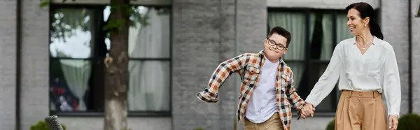 A mother walks her son with Down syndrome outdoors near an office building, showcasing diversity and inclusion. — Stock Photo