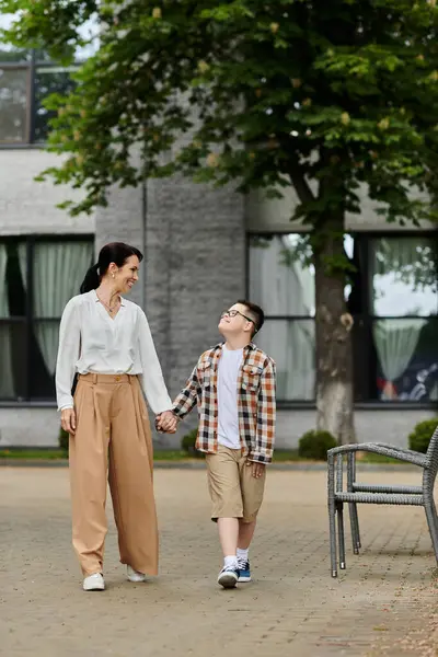 A mother walks hand-in-hand with her son, who has Down syndrome, near an office building. — Stock Photo