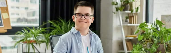 A young boy with Down syndrome smiles at the camera while sitting at a desk in his home office. — Stock Photo