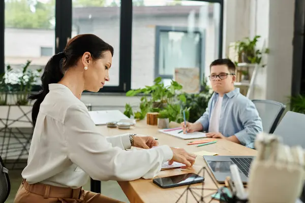 Mother works while son with Down syndrome draws nearby, emphasizing importance of diversity and inclusion at work. — Stock Photo