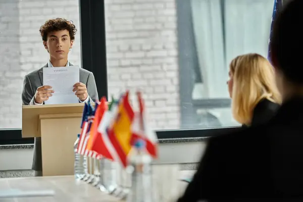 Teenage boy delivers a speech at a UN Model conference, surrounded by international flags. — Stock Photo