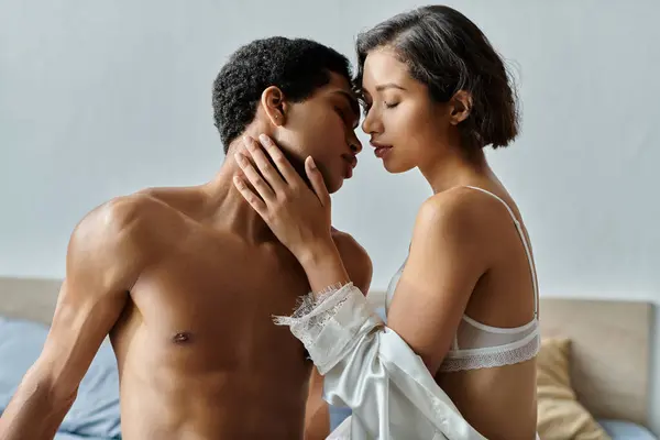 Uma jovem mulher asiática e homem afro-americano abraçar e beijar intimamente em uma cama. — Fotografia de Stock