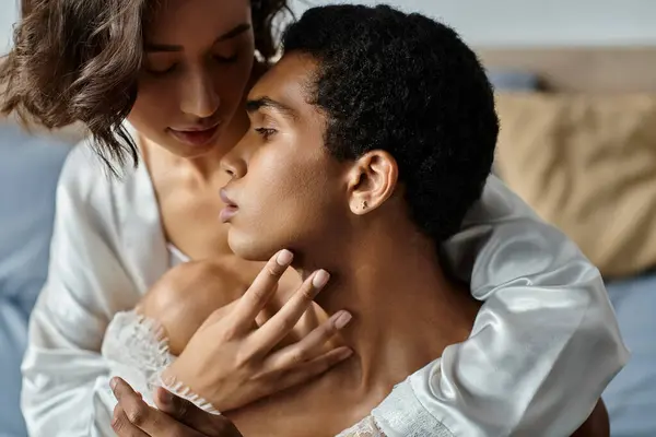 An Asian woman and an African American man embrace on a bed, their eyes locked in a tender moment. — Stock Photo