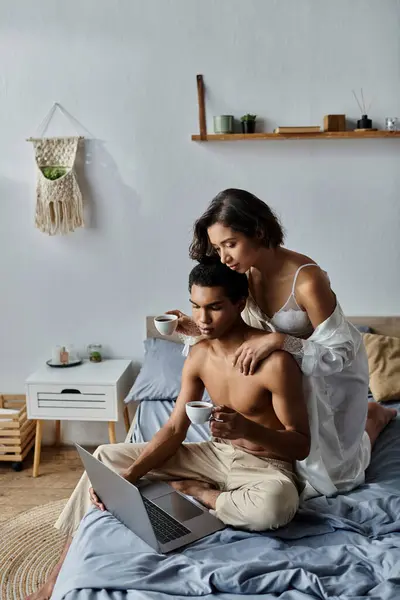 A young couple enjoys a cozy morning together in their bedroom, sipping coffee and browsing on a laptop. — Stock Photo