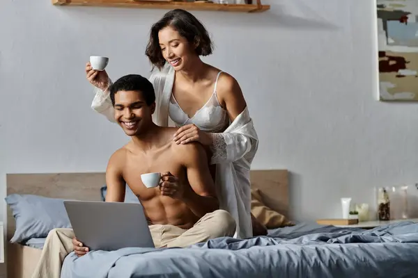 Um jovem casal gosta de café e um laptop na cama. — Fotografia de Stock