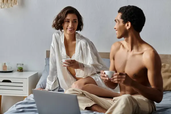 A young interracial couple enjoys a cup of coffee and some quality time together in their bedroom. — Stock Photo