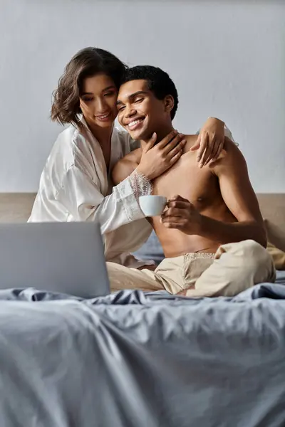 Um jovem casal se abraça na cama, desfrutando de uma manhã de café e laptop. — Fotografia de Stock