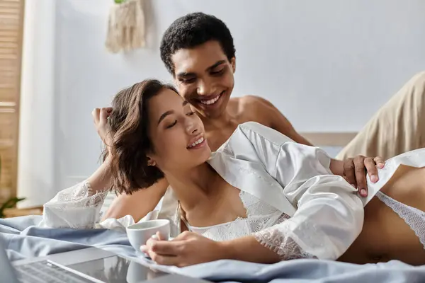 A young couple, one Black and one White, share a cozy morning moment in their bedroom. — Stock Photo