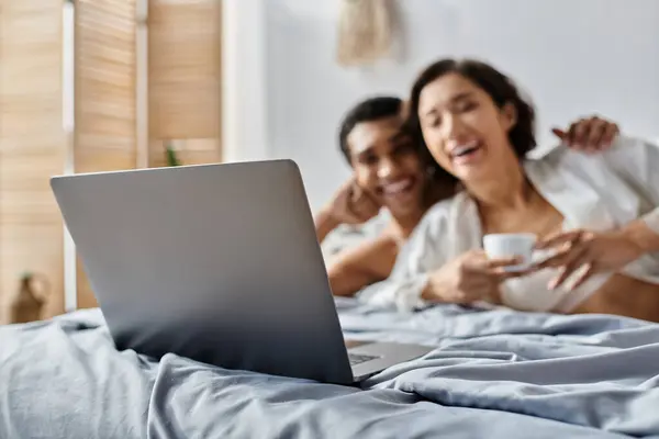 A multicultural couple enjoys a relaxing morning together in bed, laughing and enjoying a cup of coffee. — Stock Photo