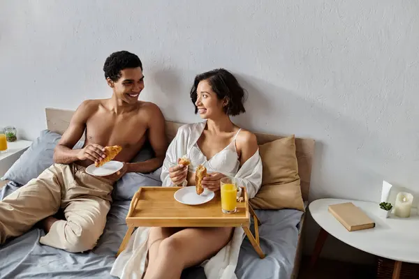 A young, multicultural couple enjoys a leisurely breakfast in bed together. — Stock Photo