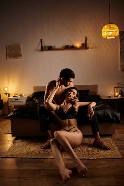 A young Asian woman in black lingerie seduces an African American man on a bed in a dimly lit bedroom. — Stock Photo