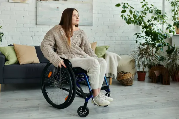 A young woman sits in a wheelchair at home, looking thoughtfully toward the window. — Stock Photo