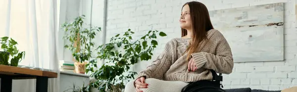 Eine junge Frau im Rollstuhl sitzt zu Hause und blickt mit nachdenklicher Miene aus dem Fenster.. — Stockfoto