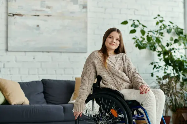 Eine junge Frau im Rollstuhl sitzt in einem Wohnzimmer und blickt gelassen in die Kamera. — Stockfoto