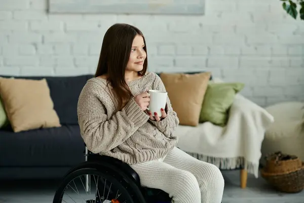 Eine junge Frau im Rollstuhl sitzt in ihrem Wohnzimmer und genießt eine Tasse Kaffee. — Stockfoto