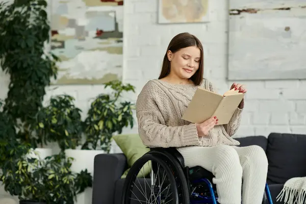 Eine junge Frau im Rollstuhl genießt einen Moment der Ruhe, während sie in ihrem Wohnzimmer ein Buch liest. — Stockfoto