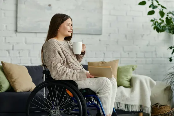 Eine Frau sitzt zu Hause im Rollstuhl und genießt eine Tasse Kaffee, während sie nachdenklich aus dem Fenster schaut. — Stockfoto