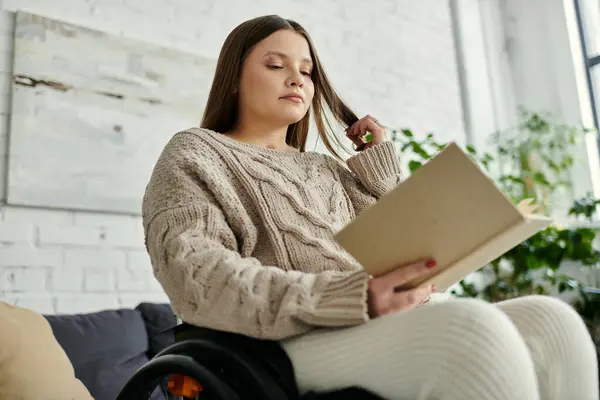 Eine junge Frau im Rollstuhl liest zu Hause ein Buch. — Stockfoto
