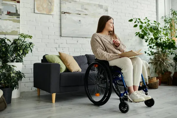 Eine junge Frau im Rollstuhl liest zu Hause ein Buch, umgeben von Pflanzen und Kunst. — Stockfoto