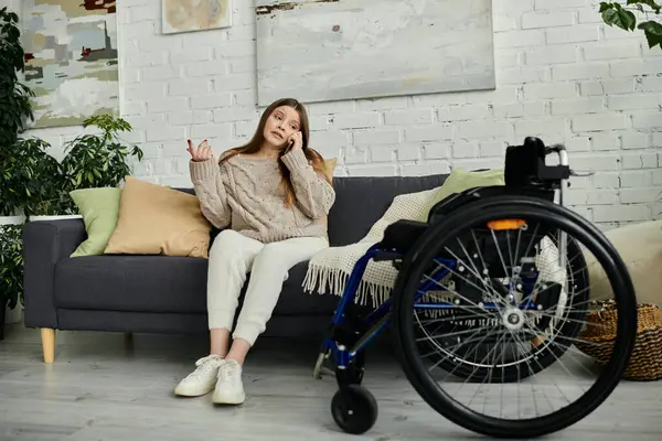 Eine junge Frau im Rollstuhl sitzt auf einer Couch und telefoniert. — Stockfoto