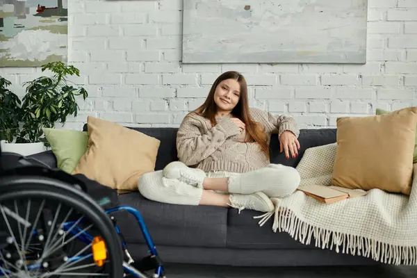 Eine junge Frau im Rollstuhl sitzt gemütlich auf einer Couch in ihrem Wohnzimmer. — Stockfoto