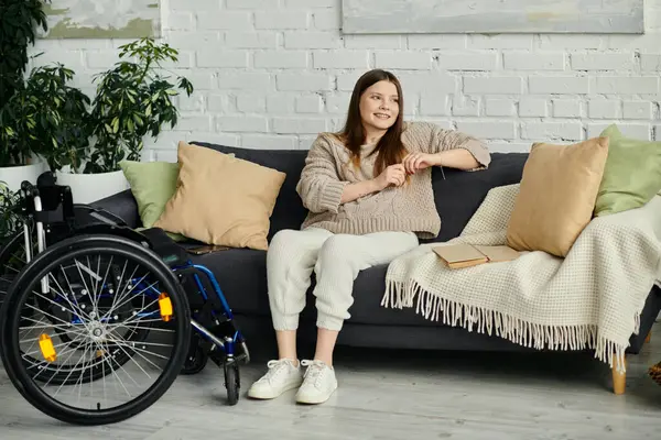A young woman in a wheelchair sits on a couch in her living room, looking relaxed and comfortable. — Stock Photo