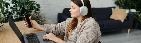 Eine junge Frau sitzt zu Hause im Rollstuhl und benutzt Laptop und Smartphone. — Stockfoto