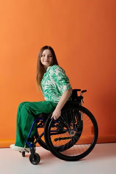 Eine selbstbewusste junge Frau im hellgrünen Outfit sitzt im Rollstuhl vor leuchtend orangefarbenem Hintergrund und lächelt strahlend. — Stockfoto