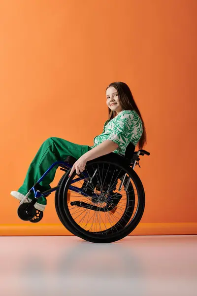 A young woman in a vibrant green outfit sits confidently in a wheelchair against a bright orange backdrop. — Stock Photo