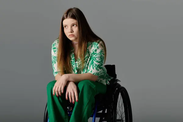 Eine behinderte junge Frau in grün sitzt elegant im Rollstuhl vor grauem Hintergrund. — Stockfoto