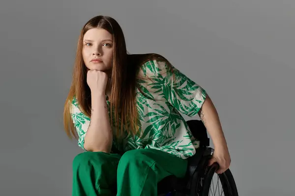 Woman in green attire sits in wheelchair looking at camera with hand on the wheel, chin resting on fist. — Stock Photo