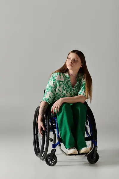 Uma jovem, vestida de verde, senta-se numa cadeira de rodas contra um fundo cinzento. — Fotografia de Stock