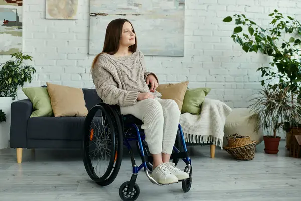 Eine junge Frau im Rollstuhl sitzt in ihrem Wohnzimmer und blickt nachdenklich in die Ferne. — Stock Photo