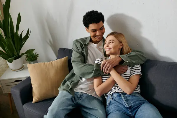 A young, multicultural couple embraces on a couch in a modern apartment. — Stock Photo